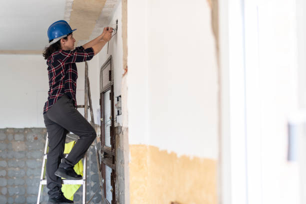 Worker installing drywall, using a ladder and tools